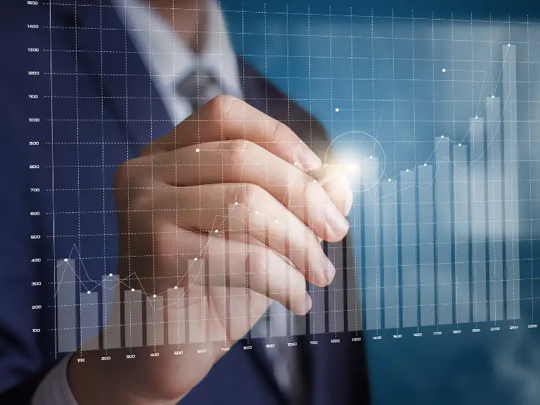 Mão de um profissional de terno escrevendo ou interagindo com um gráfico de barras e linhas digitais, projetado em um fundo escuro